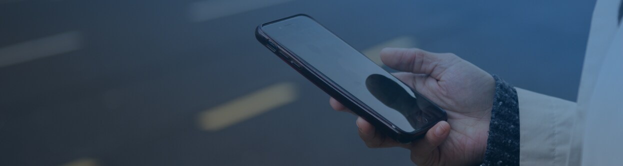 Detail osoby stojící na kraji silnice a rolující na mobilu, překrytý modrým přechodem